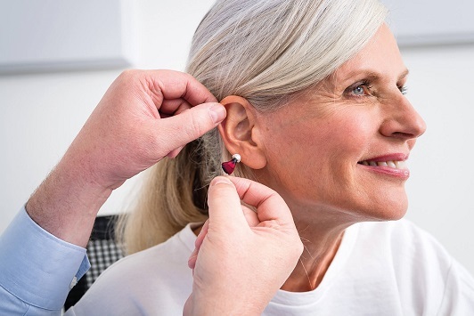 Ältere Frau bekommt modernes Hörgerät eingesetzt, Hörakustik und Hörhilfe Beratung.